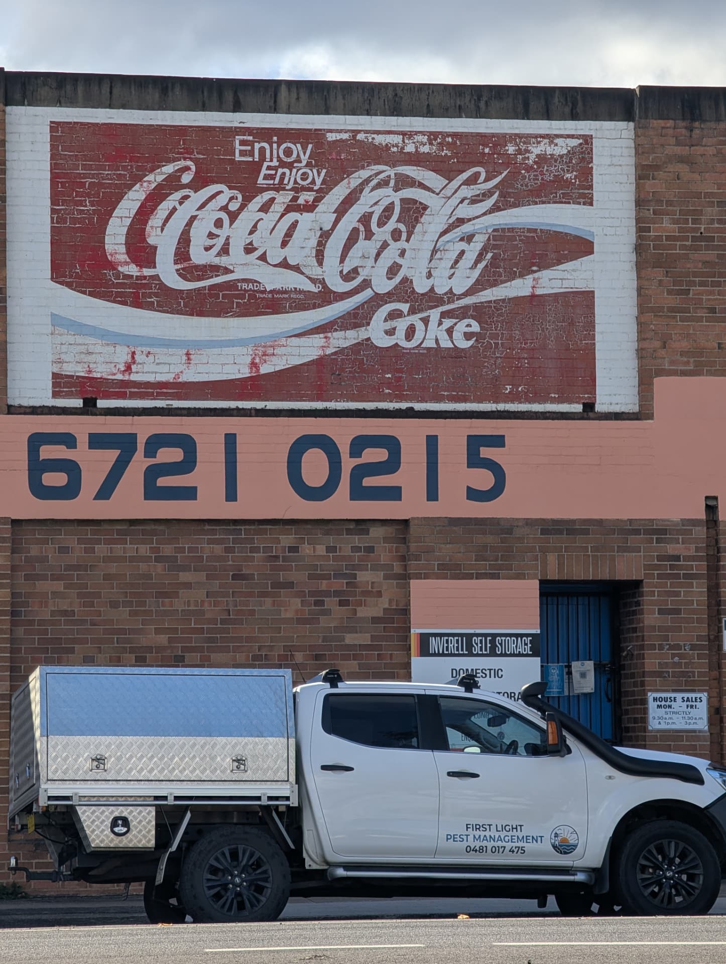 The First Light ute parked beneath a faded vintage Coca-Cola mural painted on a brick wall in Inverell